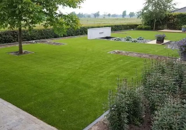 Großer Garten mit verlegtem Kunstrasen, niedriger Buchshecke und Blick auf offene Felder