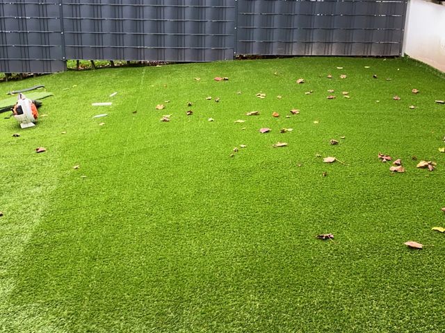 Kunstrasenfläche mit heruntergefallenem Herbstlaub und einem abgelegten Besen