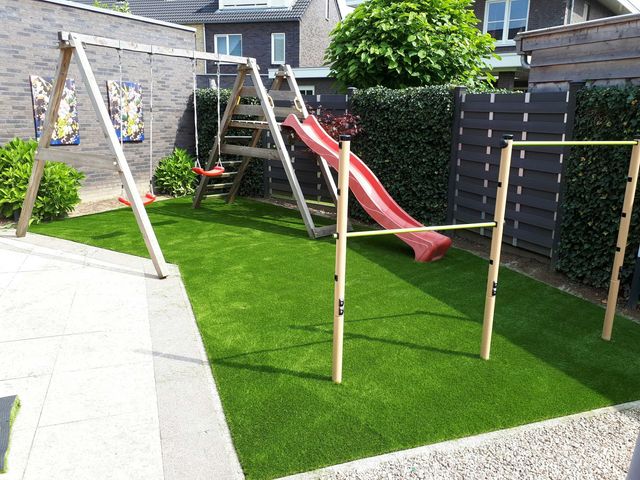 Garten mit Schaukel und Rutsche auf Kunstrasen, eingefasst von Hecke und Sichtschutzzaun