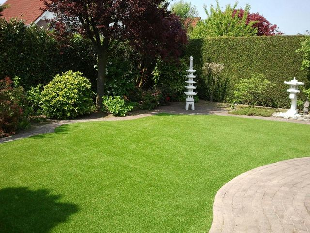 Garten mit Kunstrasen, geschwungenem Plattenweg, Steinlaternen und blühenden Sträuchern