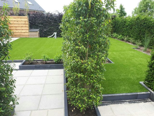 Kunstrasenfläche im Garten zwischen hohen Heckenpfeilern und niedrigen Pflanzkübeln