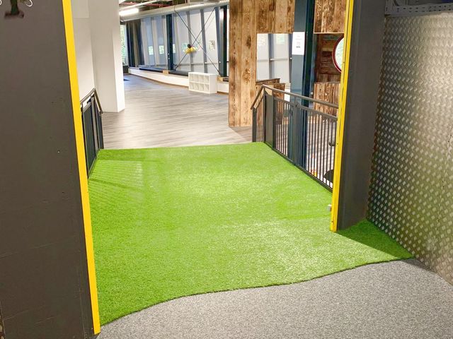 Eingangsbereich eines Fitnessstudios mit Kunstrasenfläche neben der Treppe