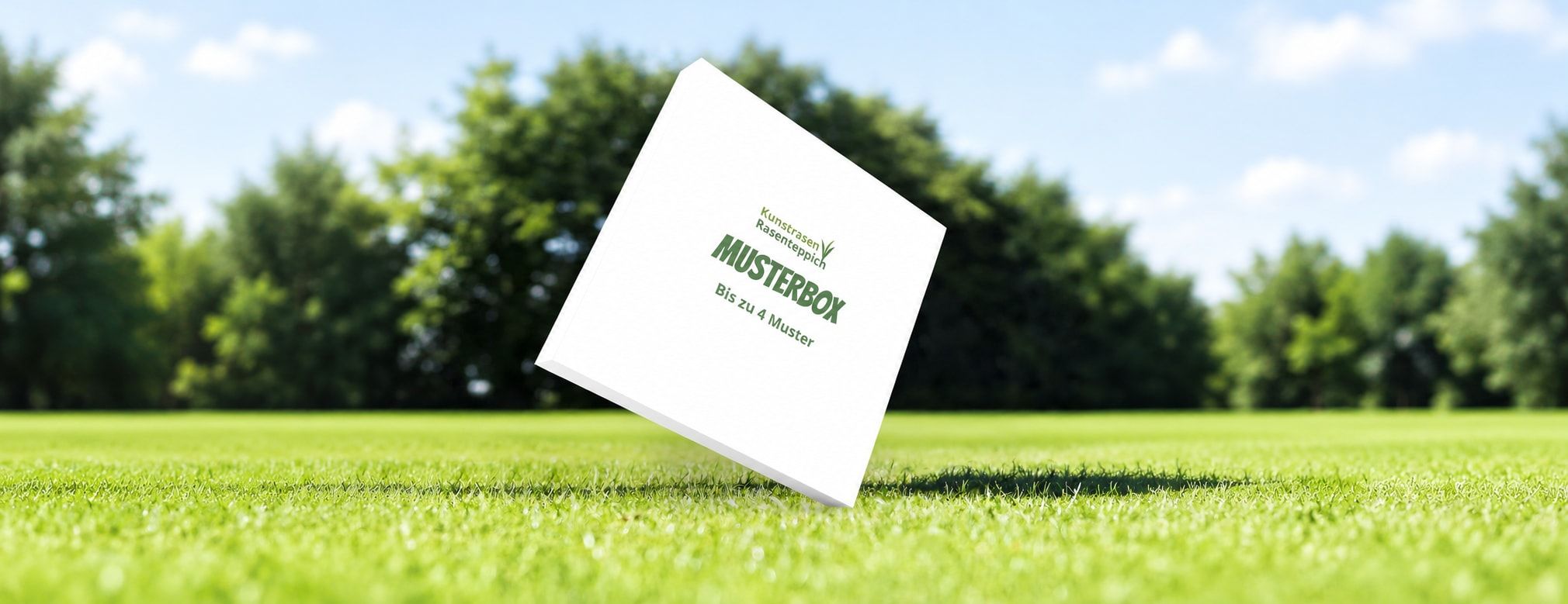 Weiße Musterbox mit dem Aufdruck „Bis zu 4 Muster“ auf einer Rasenfläche, dahinter Bäume und blauer Himmel