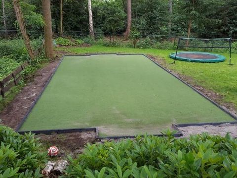 Rechteckige Spielfläche aus Kunstrasen im Garten, dahinter ein Trampolin