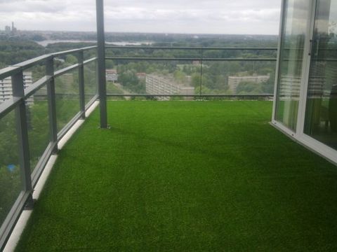 Balkon mit Kunstrasen und Glasgeländer, dahinter der Blick über die Stadt