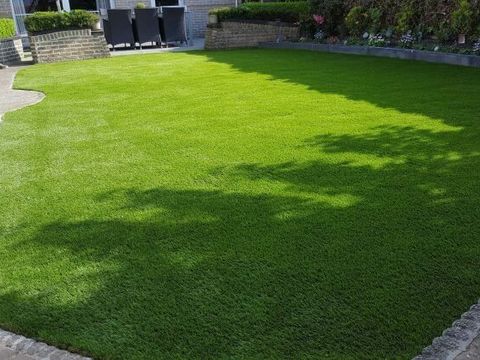 Kunstrasenfläche im Garten mit Natursteinmauer und Gartenmöbeln