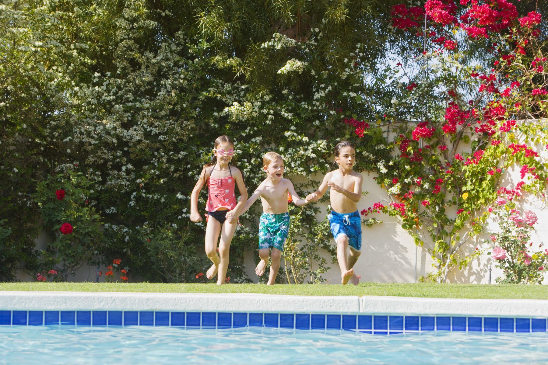 Drei Kinder laufen an einem Pool entlang