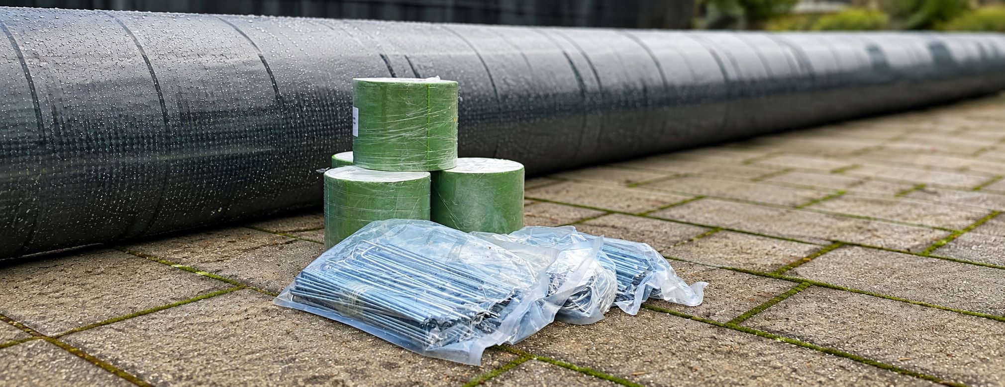 Verlegematerial neben einer Kunstrasenrolle: Nahtbandrollen und verpackte Erdnägel